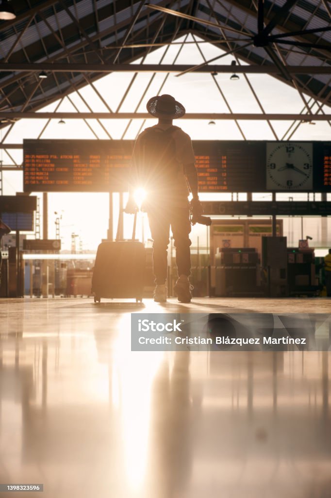 Silhouette of a man wearing a hat and carrying a suitcase looking at a destination travel panel Airport Stock Photo