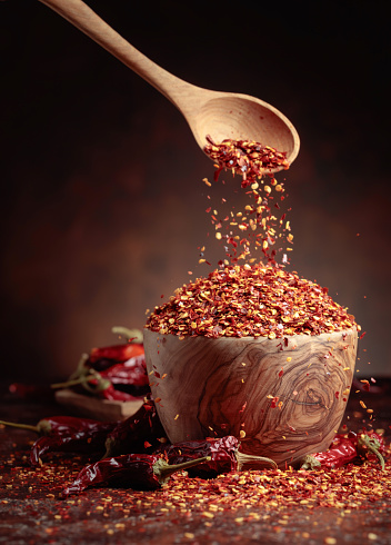 Chilli flakes are poured into a wooden dish. Chilli flakes and dried chili peppers on a brown background.