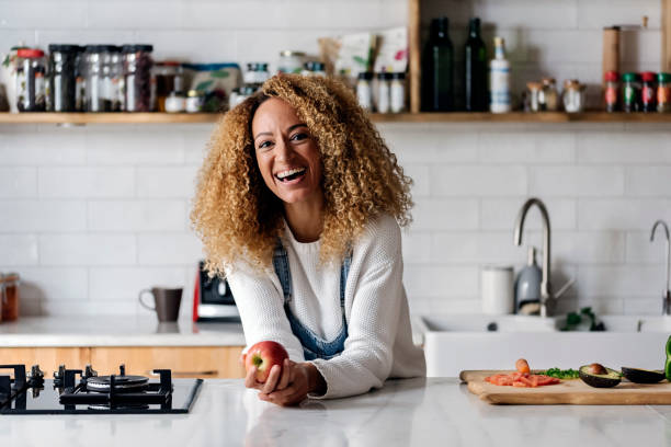 Portrait of a woman in the kitchen. Stock photo of a middle aged woman holding an apple in a kitchen. She is smiling and looking at camera mid adult stock pictures, royalty-free photos & images
