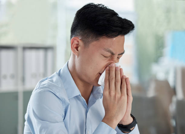 One sick asian businessman blowing runny nose with tissue while working in an office. Guy feeling unwell with flu, cold and covid symptoms. Suffering with congestion, sinus and seasonal spring allergy un hombre de negocios asiático enfermo que se sonó la secreción nasal con pañuelos de papel mientras trabajaba en una oficina. chico que se siente mal con síntomas de gripe, resfriado y covid. sufrir de congestión, sinusitis y alergia estacional de p