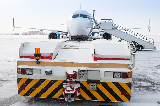 Tow truck pulls up to the passenger aircraft with boarding steps in a blizzard