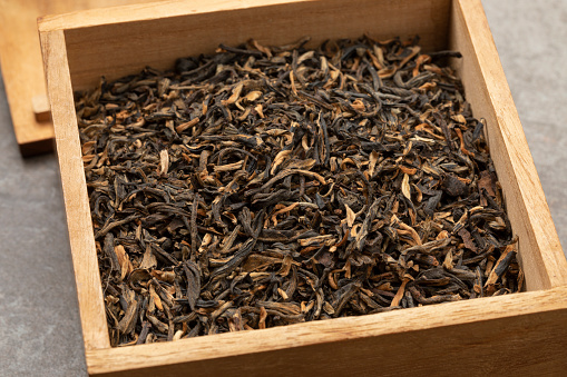 Wooden box with dried Chinese Yunnan Mao Feng tea close up