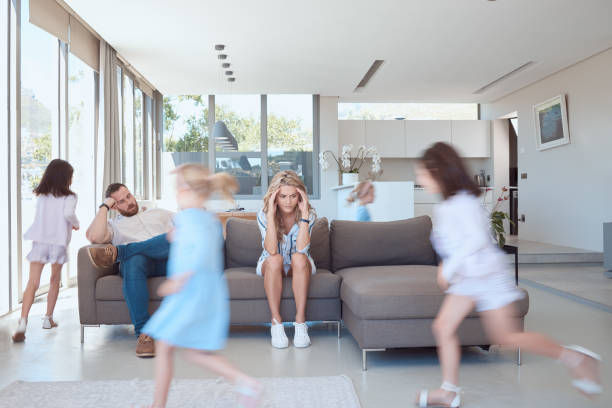 istock Exhausted mother and father looking stressed, while children run around playing in the lounge. Upset parents with headache siting on the couch, children playing around them. Young girls playing 1398334377
