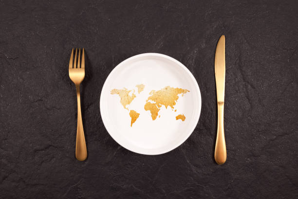 Bread in shape world map on white plate. Gold fork and knife on a dark stone background. Abstract Concept of global hunger.