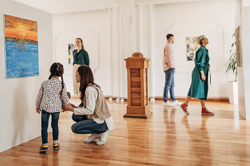 Low angle view of a beautiful Caucasian family at a sculpture expo. Full length image, all smiling while the man and the boy are taking a step closer to the pedestal. Large space around them.