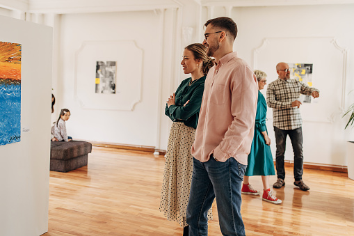 Diverse group of visitors in modern art gallery looking at paintings