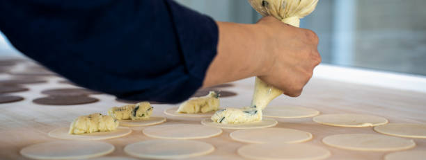 Horizontal banner or header with woman prepare fresh made ravioli inside pasta factory. Using a pastry bag or sac a poche to make stuffed pasta ravioli, culurgiones, agnolotti. Focus on stuffed