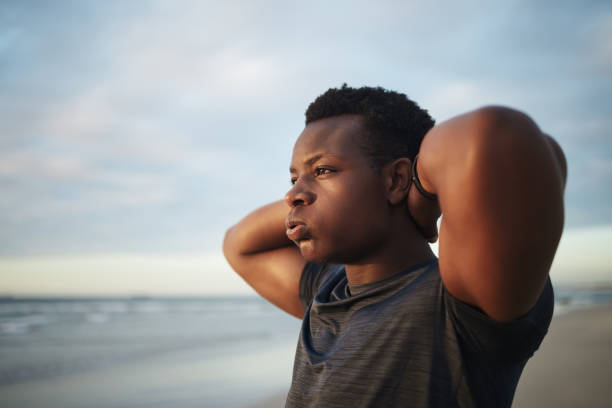 close-up tiro de um homem africano-americano muscular parecendo preocupado e ansioso enquanto se exercitava na praia. black fit masculino estressado ao fazer exercício de aquecimento cardio durante uma sessão de treino - tired men african descent sadness - fotografias e filmes do acervo