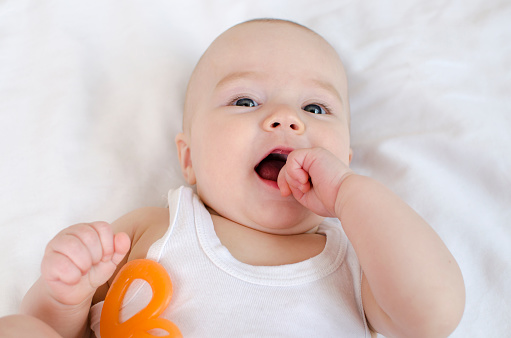 The baby grows the first tooth. Cute newborn, biting teether in bed close-up
