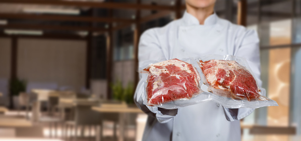 The cook shows the meat packed vacuum packaging on a blurred background.