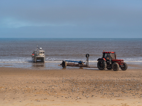 A fisherman reversing his trailer down to the surf to collect his crab fishing boat in Cromer, Norfolk, Eastern England, after a morning’s fishing. A sea mist is rolling in on the horizon.