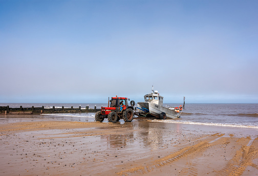Cromer, Norfolk, Eastern England, where a fisherman is using an old tractor to drag his crab boat from the surf after a morning’s fishing. A thick sea mist lurks on the horizon.