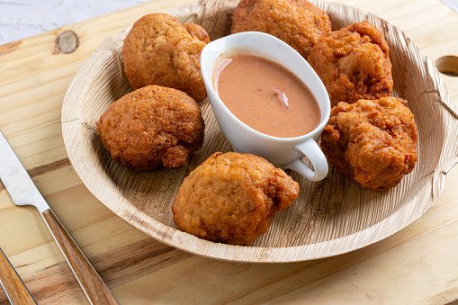 Nigerian snack known as Akara served with dipping in a wooden plate on a wooden table with fork and knife