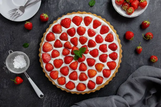 Delicious strawberry tart with whipped cream and mascarpone on a dark concrete background. Top view.