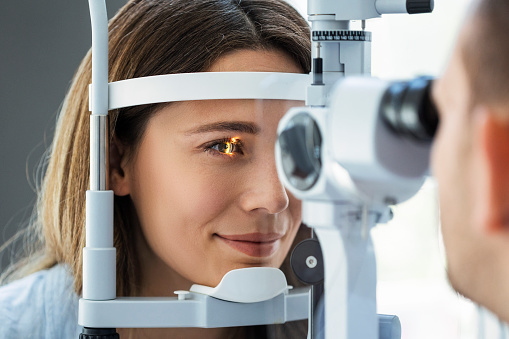 Shot of young woman sitting on chair with beautiful optician standing while doing eye test in ophthalmology clinic.