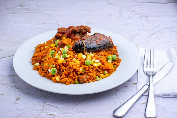 Jollof rice and veggies with goat meat Nigerian jollof rice with goat meat served on a white plate with cutleries. fork silverware table knife fine dining stock pictures, royalty-free photos & images