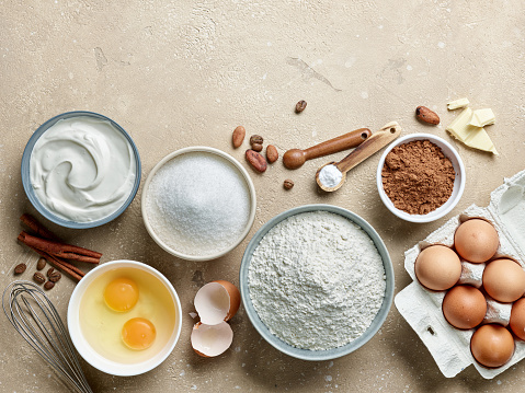 various baking ingredients on beige color table background, top view