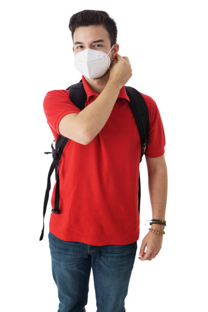 Young man putting on face mask behind ear and looking at camera, posing against a white background.