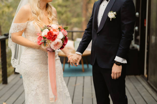 Wedding couple holding hands outdoors Recently married couple during an outdoor elopement ceremony. Holding hands with a bouquet of flowers and patio background. Evokes feelings of happiness, romance and love. eloping stock pictures, royalty-free photos & images