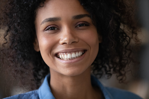 Close up head shot happy young African American woman with perfect white toothy smile skin looking at camera, feeling satisfied with professional dental procedure, profile portrait photo of client.