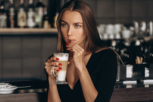 Young beautiful smiling woman enjoying latte in cafe