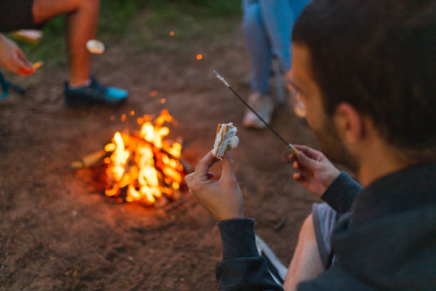 istock Close-up of a young man making a marshmallow sandwich while camping outdoors with friends 1398377300