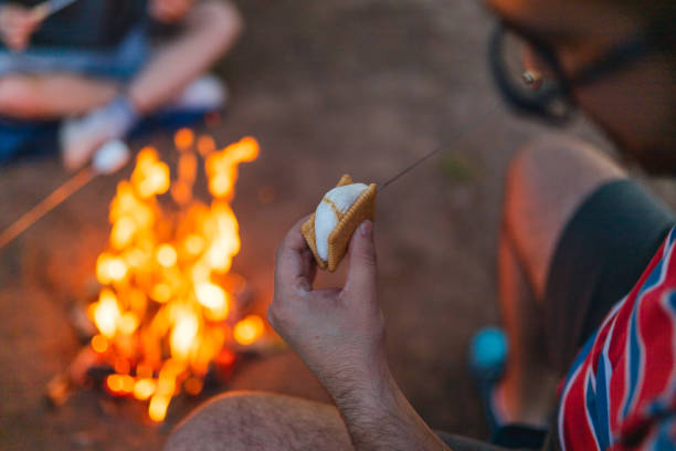 istock Close-up of a young man making a marshmallow sandwich while camping outdoors with friends 1398377356