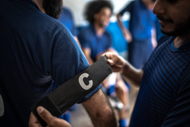 Soccer player helping team captain putting on arm band
