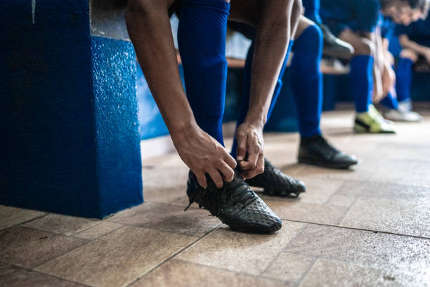 giocatore di calcio che lega i lacci delle scarpe mentre si prepara per la partita nello spogliatoio - spogliatoio foto e immagini stock