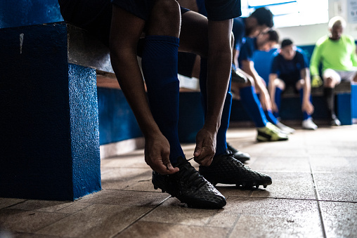 Soccer player tying shoelaces while preparing for match in the locker room