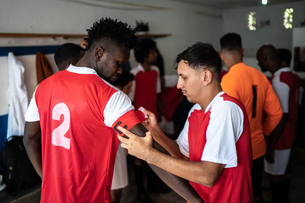 istock Soccer player helping the team captain getting ready before a match in the locker room 1398379529