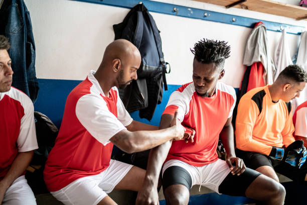 istock Soccer player helping the team captain getting ready before a match in the locker room 1398379595