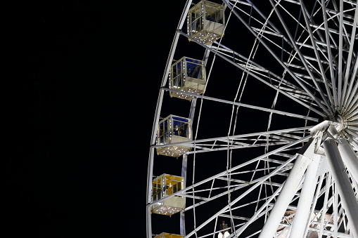 Illuminated white Ferris wheel against the black night sky. Part of the wheel with copy space