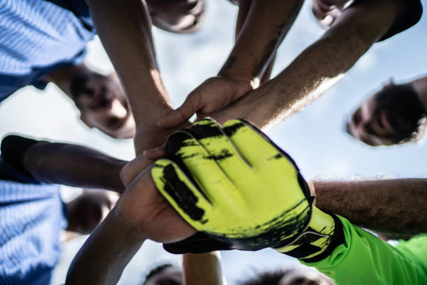 Low angle shot of a group of sports team forming a huddle with their hands outdoor. Sports team stacking hands together before the game