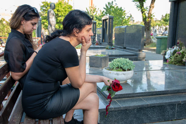 어머니와 딸이 슬픔에 잠겨 공동 묘지에서 죽은 사랑하는 사람을 애도하고 있습니다. - cemetery child mourner death 뉴스 사진 이미지
