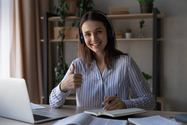 Happy business school student girl recommending training course Happy business school student girl recommending training course, satisfied with online learning quality. Woman in headphones smiling, showing like thumb up at camera at laptop. Head shot portrait online tutors stock pictures, royalty-free photos & images