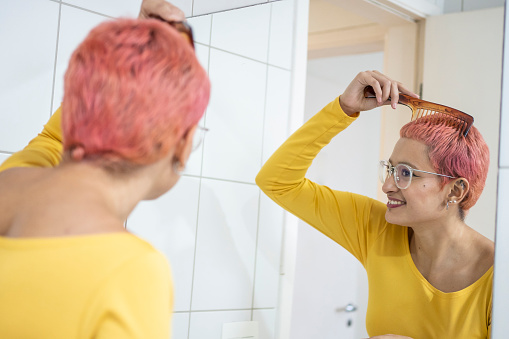 Non-binary person combing hair in bathroom mirror