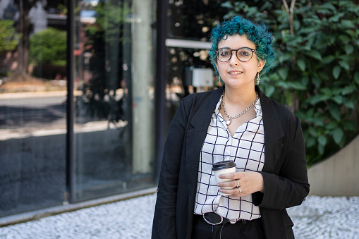 Portrait of young woman with green hair with smart phone outside the office building