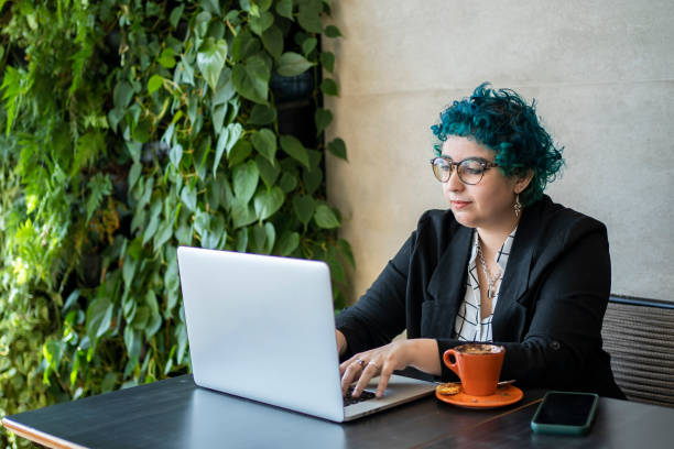 Young woman with green hair working on computer in cafe stock photo