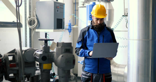 A waist view of a worker in a heating plant using a laptop.