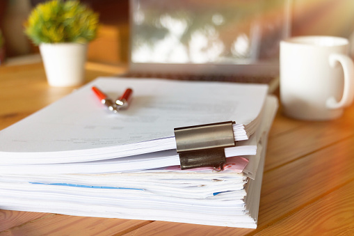 paperworks with black paperclips on top on wooden table in office with office supplies