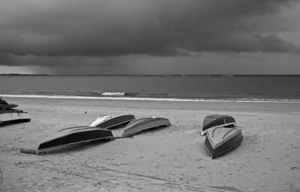 Boats upside down on a sandy beach.  Storm clouds in the distance with rain.  Black and white photograph near Natal, Brazil (Brasil).