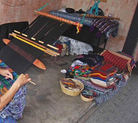 A Guatemalan woman at her work area.   Guatemalan fabric.  Weaving instruments and woman's hands.  Unrecognizable person.