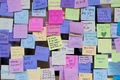 Colorful sticky notes with a variety of messages and emojis on a storefront window at a university campus before graduation day.
