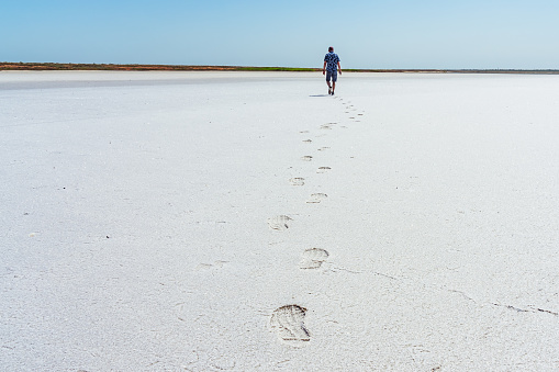 A walking tourist and his footprints on the dried salt on the shore of the sea bay