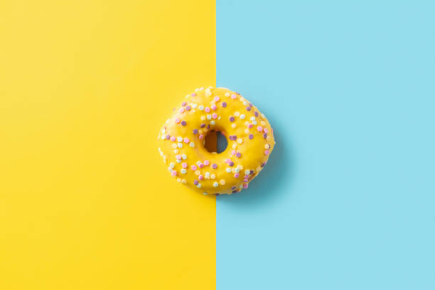 istock Yellow donut covered with icing and colorful sprinkles, top view on trendy two colored blue and yellow background. Flat lay style, space for text 1398433630