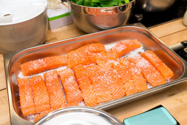 Metal tray with raw salmon fillets under coarse salt. Salted before cooking. stock photo