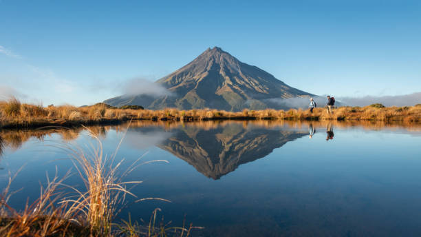 dwie osoby wędrujące po torze pouakai. góra taranaki odbita w tarn we wczesnym porannym słońcu - nowa zelandia zdjęcia i obrazy z banku zdjęć