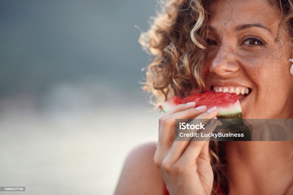 Beautiful young woman with curly hair biting on watermelon piece. Summertime, holiday, lifestyle concept. Beautiful young woman with curly hair biting on watermelon piece. Summertime, lifestyle concept. Eating Stock Photo