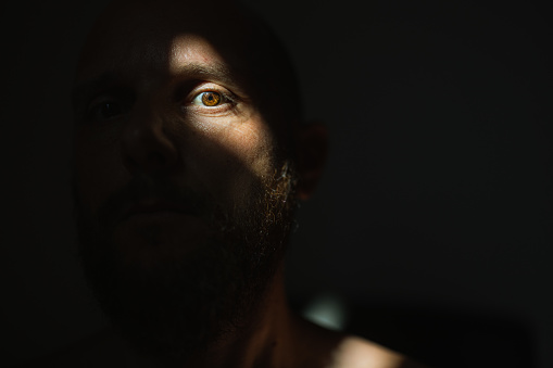 Dramatic light self portrait: bearded man in the shadow. Half of the face is illuminated by sunlight, the other is in the dark